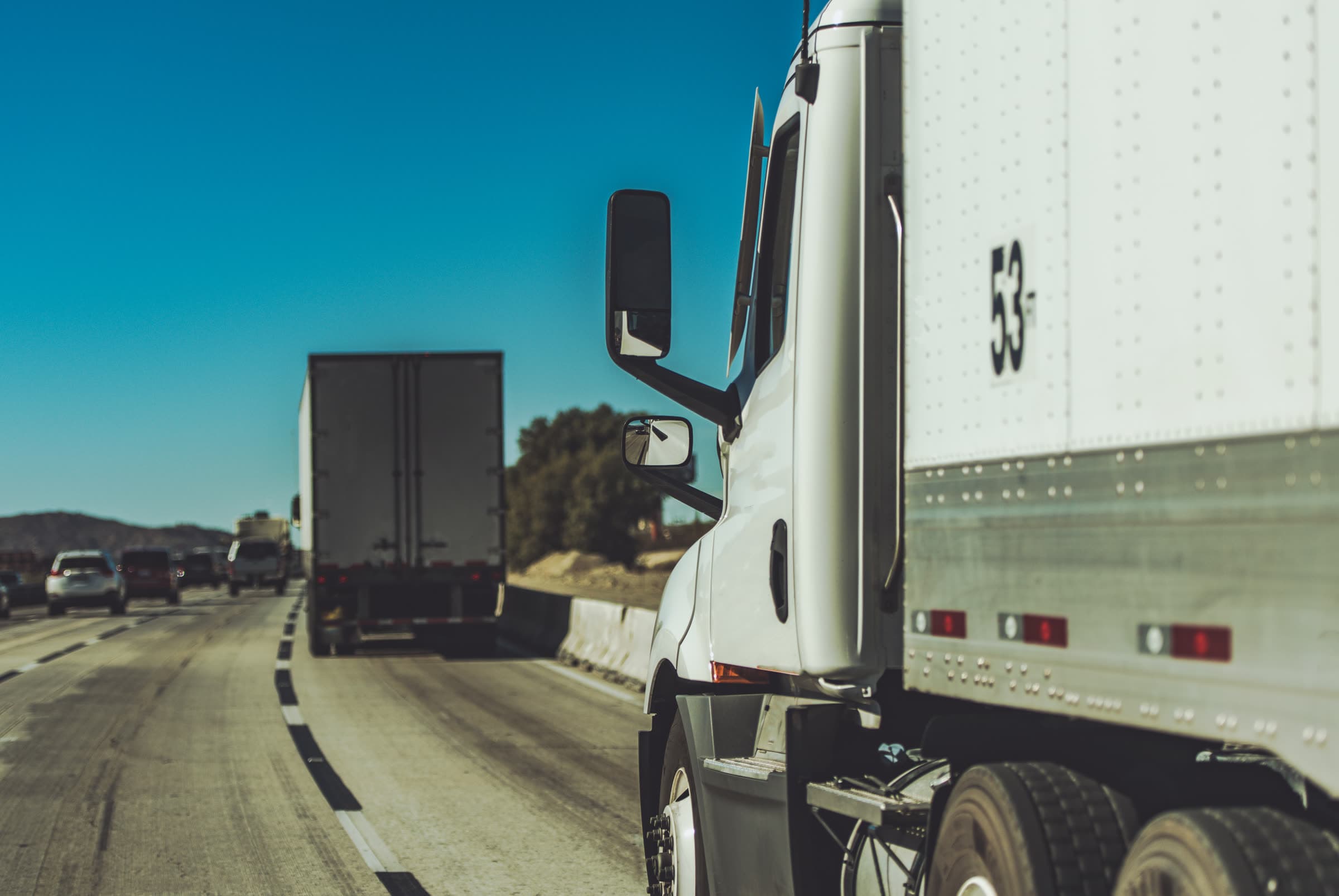 A 53-foot semi-truck on a California interstate highway in a convoy with other trucks